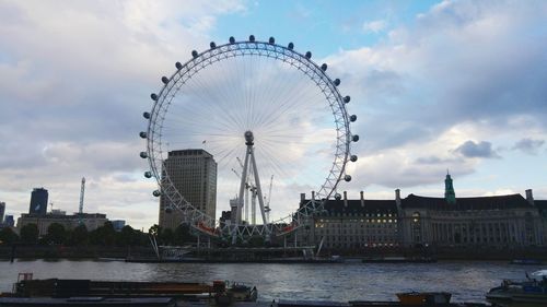 Low angle view of ferris wheel by river against sky