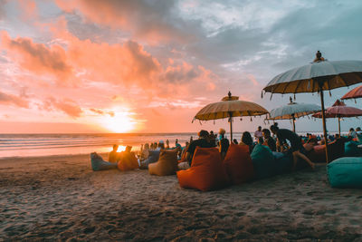 People relaxing on beach against sky during sunset