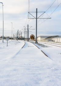 Railway in snow covered field against sky