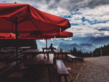 Benches and parasols by mountains against cloudy sky