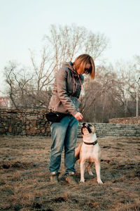 Full length of woman looking at dog while standing on field