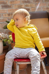 Cute baby girl looking away while sitting on chair