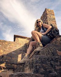 Portrait of woman sitting on rock against sky