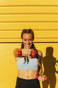 Young woman smiling while standing against yellow wall