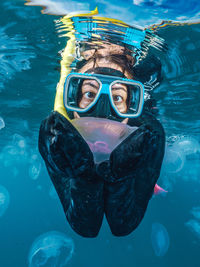 A woman in a black wetsuit is in the water with jellyfish. the jellyfish are floating around her