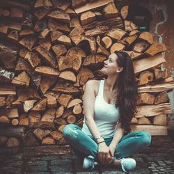 Beautiful smiling woman sitting against stack of logs in warehouse