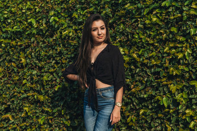 Portrait of young woman standing against plants