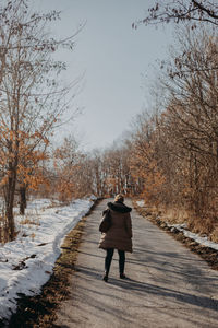 Rear view of woman walking on snow covered road