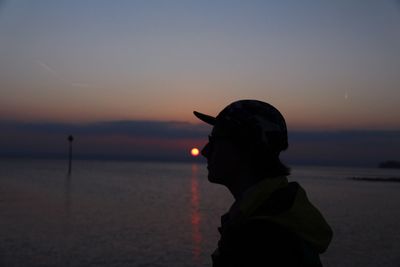 Side view of silhouette man at seashore against sky during sunset