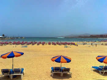 Lounge chairs and parasols on beach against blue sky