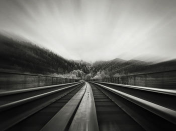 Black and white scene, motion, of an old railway bridge piercing the forest through the mountains