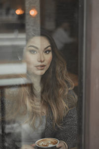 Portrait of beautiful woman sitting at cafe seen through glass
