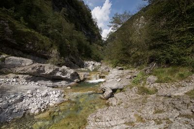 Stream flowing through rocks by river against sky