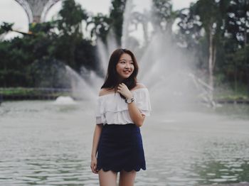 Smiling young woman standing against fountain at park