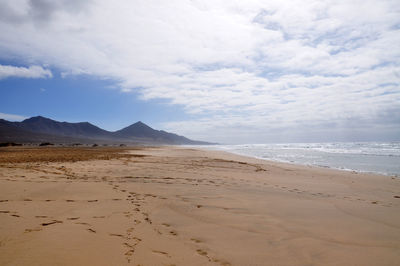 Scenic view of sandy beach against cloudy sky