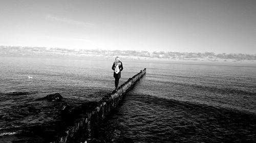 Rear view of woman walking on groyne amidst sea