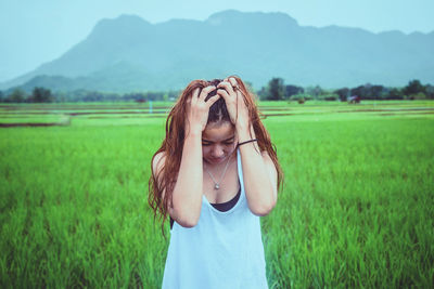 Beautiful woman standing on field with hand in hair against sky