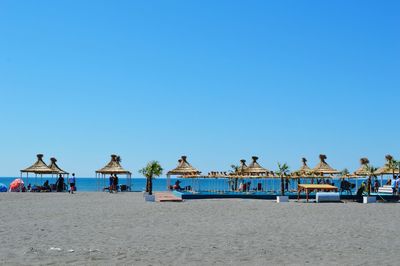 People at beach against clear blue sky