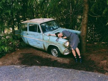 Smiling woman leaning on abandoned car hood at roadside