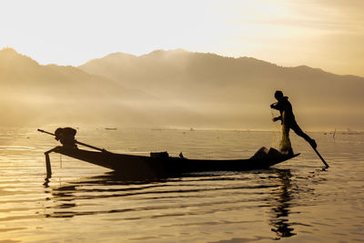 Side view of silhouette man on boat in sea against sky