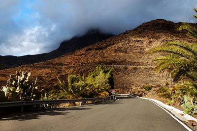 Diminishing perspective of road passing through mountains against cloudy sky