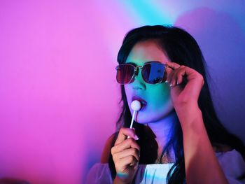 Beautiful woman eating lollipop while wearing sunglasses in illuminated room