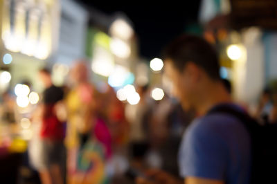 Rear view of people standing on illuminated street at night