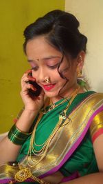 Smiling girl in sari looking down while using mobile phone at home