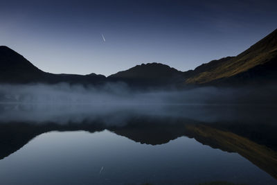 Scenic view of lake by silhouette mountains against sky