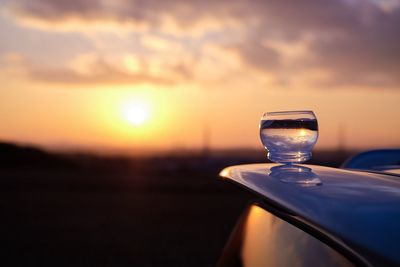 Close-up of drink on car roof against sky during sunset