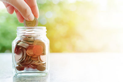 Cropped hand putting coins in jar on table