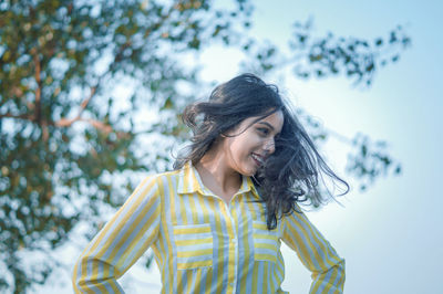 Smiling young woman looking away against trees