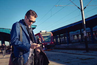 Handsome man using phone at railroad station platform