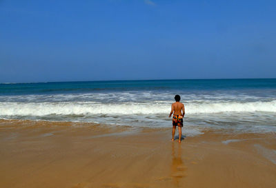 Rear view of shirtless man walking at beach against sky