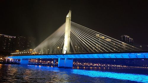 Illuminated bridge over river against sky at night