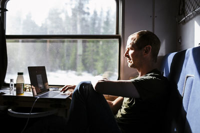 Businessman using laptop while sitting by window in train