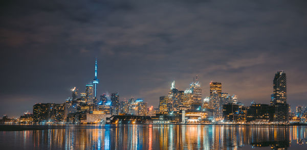 Illuminated buildings in city against cloudy sky