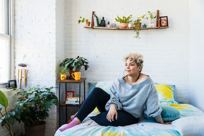 Thoughtful mid adult woman looking away while sitting on bed at home