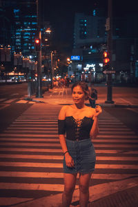 Full length portrait of young woman standing on city street at night