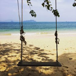 Empty swing hanging at beach against sky