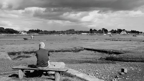 Rear view of woman sitting on beach against sky