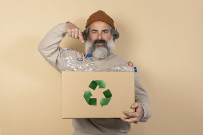 Confident man points to the box full of bottles for recycling isolated over brown background