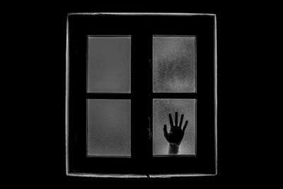 Cropped hand seen through closed glass window of house