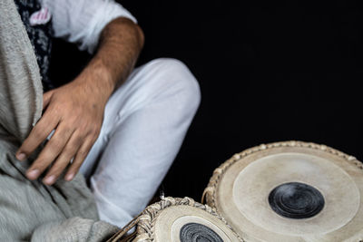 Midsection of man sitting on floor against black background