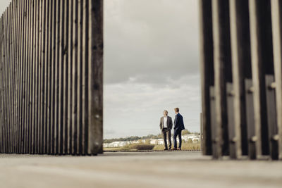 Two businessmen standing on jetty at a lake talking