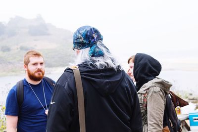 Friends hiking by mountain against sky during foggy weather