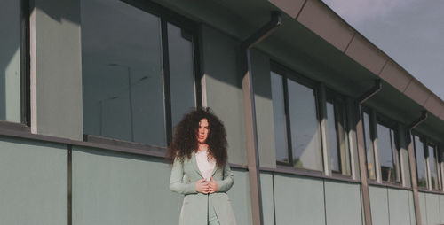 Portrait of woman with curly hair standing against building