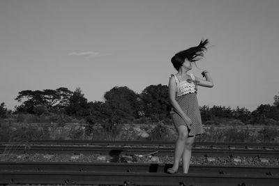 Woman tossing hair while standing on railroad track against sky