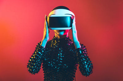 Young woman with shaved head wearing virtual reality glasses against pink background