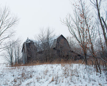 Bare trees by house against clear sky during winter